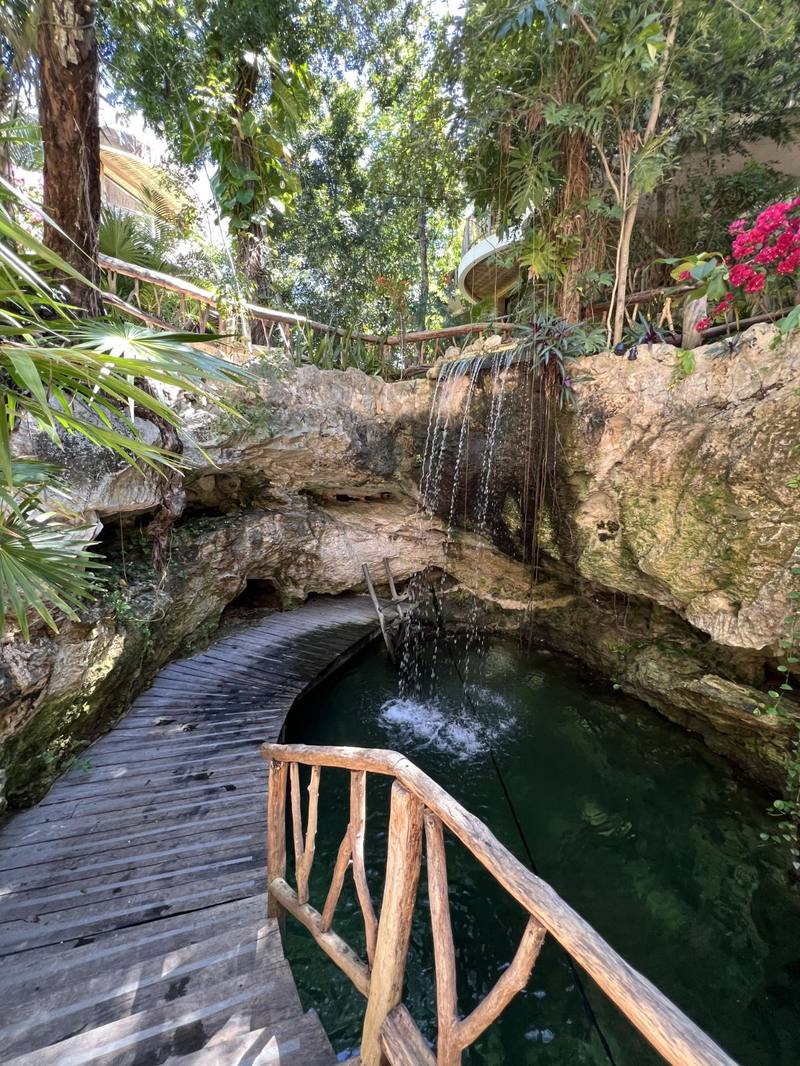 Waterfall spilling into the private cenote beside a curved boardwalk